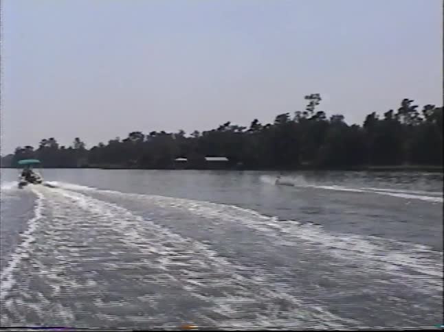 Vintage home movie footage captures a man water skiing and carving through the wake on a sunny day at the lake