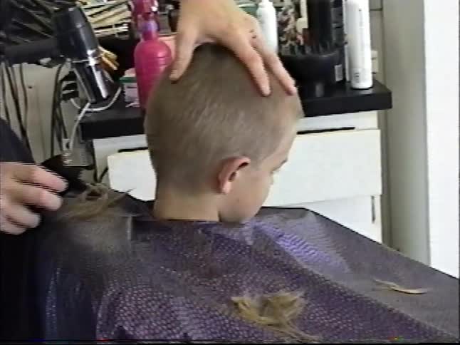 Vintage footage of a hairstylist giving a young boy a short buzz cut with scissors and electric clippers in a salon