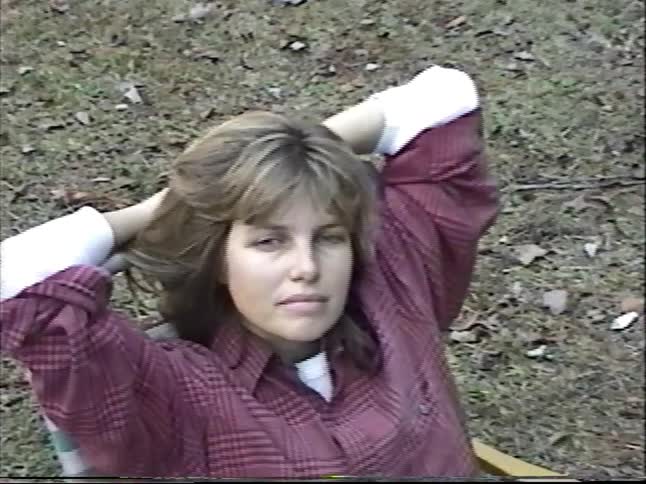 Vintage home movie captures a family and their black dog relaxing around a campfire during a camping trip