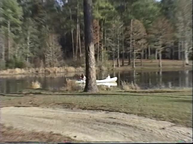 Vintage footage captures a family paddling in a canoe on a tranquil lake surrounded by a dense forest