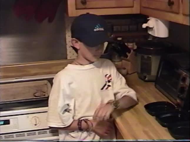 A young boy stands in the kitchen next to a freshly baked loaf of homemade bread in this vintage home video