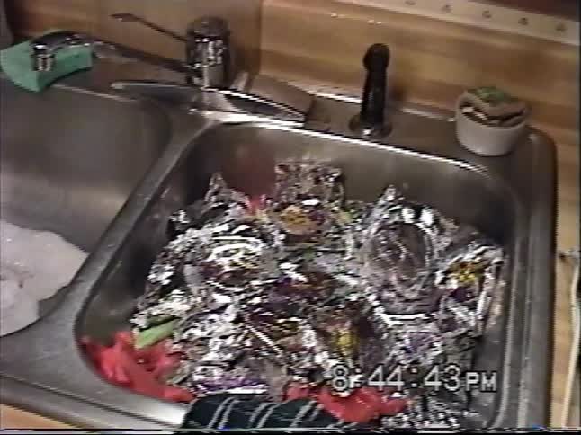 Vintage VHS footage shows a kitchen sink overflowing with shiny candy or snack wrappers