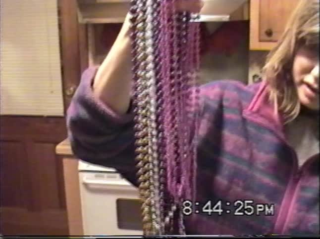 A woman shows a young boy a collection of colorful Mardi Gras beads in a home kitchen in this vintage home video