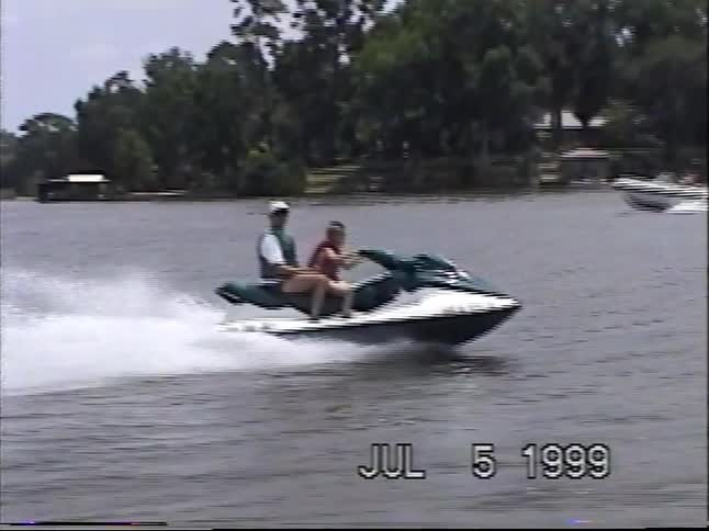 A father and son have fun riding a jet ski at speed across a lake in this nostalgic 1990s home video footage