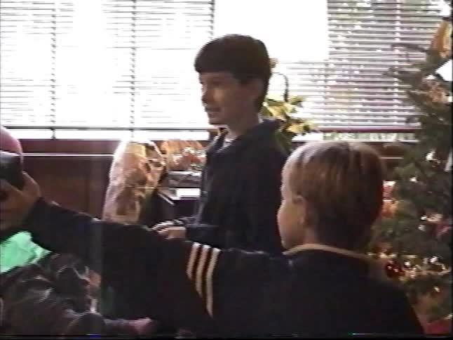 A nostalgic VHS home video captures two young brothers happily opening presents on Christmas day