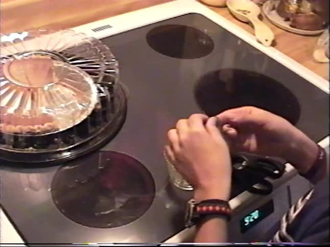 A vintage VHS recording captures a teenager working on a project in the kitchen while a friend watches