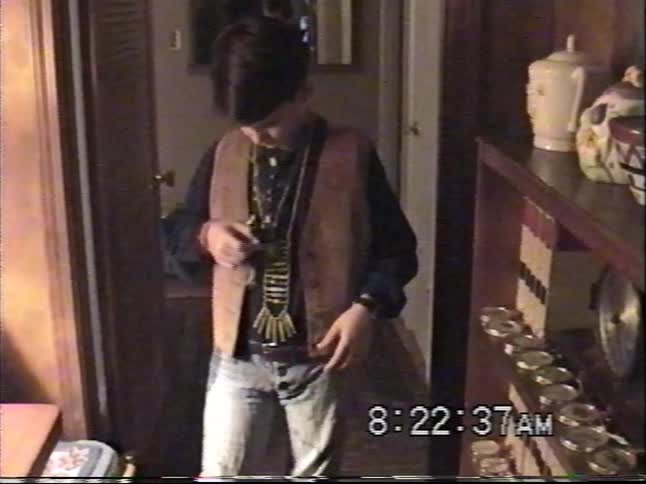 Vintage home movie captures a young boy putting on his 90s Western-style costume with a suede vest and beaded necklaces