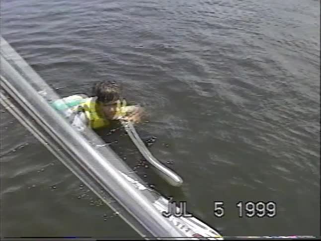 Vintage home video from 1999 captures a young boy learning to water ski, managing to stand up before taking a splash into the lake