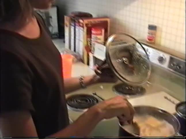 A woman cooks on the stove in her kitchen, captured in candid 1990s home video footage