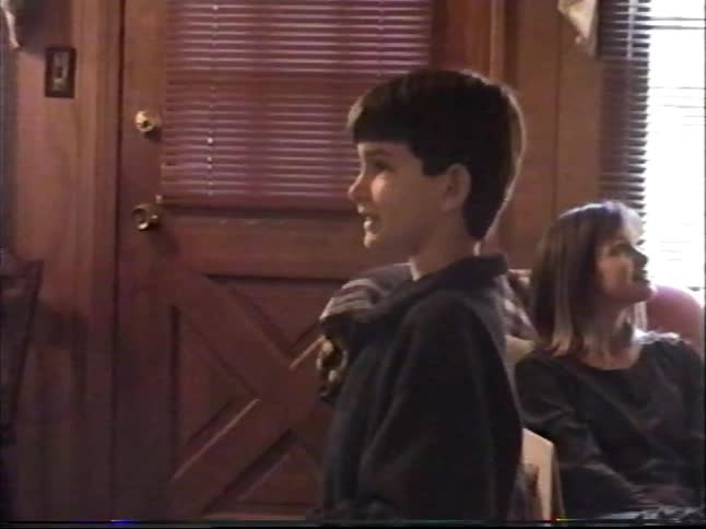 A happy young boy stands in his living room, talking and smiling with his family in this authentic 90s home video