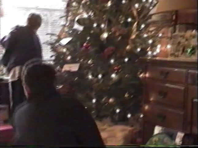 Vintage home video footage captures a family gathering in their living room on Christmas morning