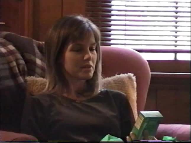 A vintage home movie captures a mother happily opening a Christmas present from her two young sons