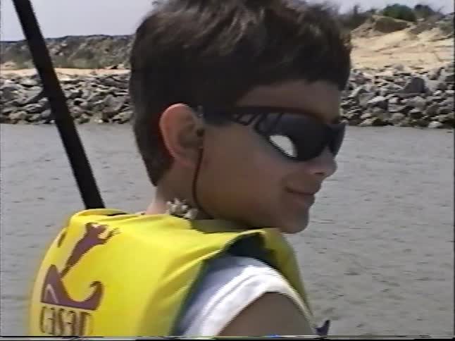 A woman and a young boy enjoy a leisurely boat trip along a rocky shoreline on a bright day