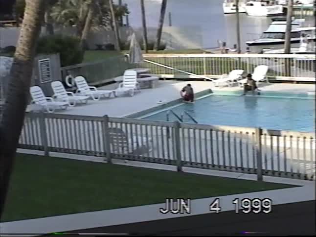A young boy uses a net to fish a toy out of a swimming pool at a marina in this vintage 1999 home video