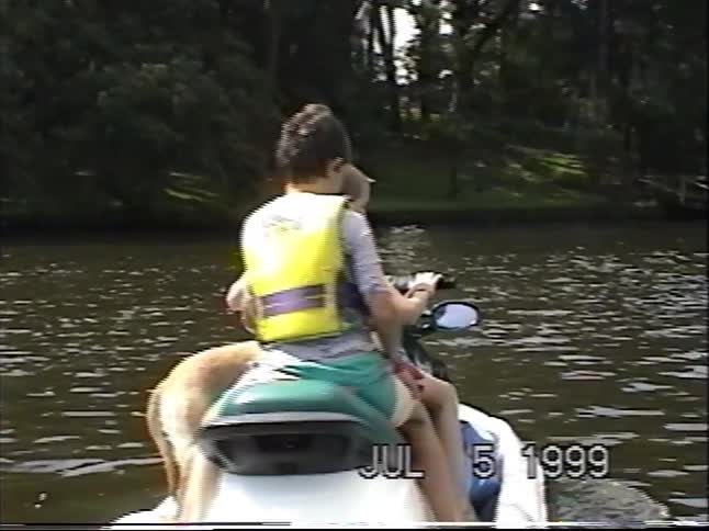 Two young boys and their dog smile for the camera while riding a jet ski on the lake in this vintage 1999 home video