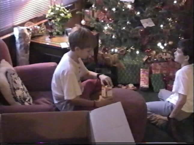 Two brothers share a happy moment opening presents by the Christmas tree in a vintage home video