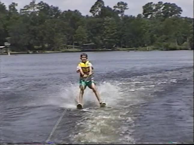 A young boy in a life vest successfully gets up on water skis and enjoys gliding across a lake on a sunny day