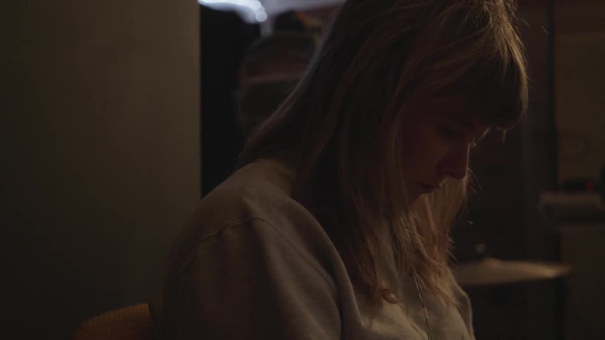 A blonde woman sits in a dimly lit room