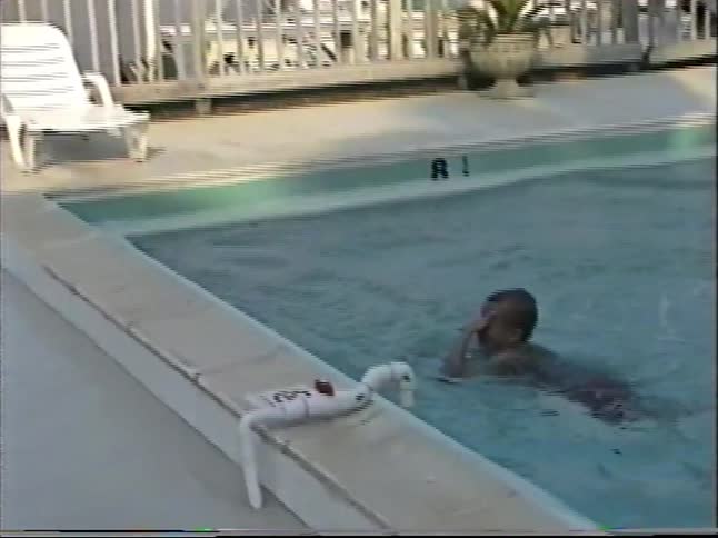 Vintage footage captures a young boy throwing dive rings into a resort swimming pool and then getting in himself