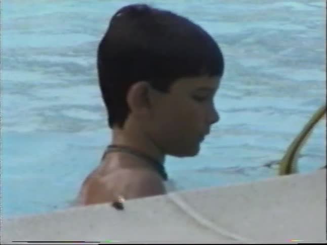 Vintage home movie captures two young boys playing and swimming in a backyard pool on a summer day