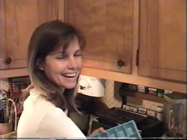 A woman and a young boy are in a home kitchen preparing what appears to be a craft involving an ice cube tray in this vintage 1999 home movie