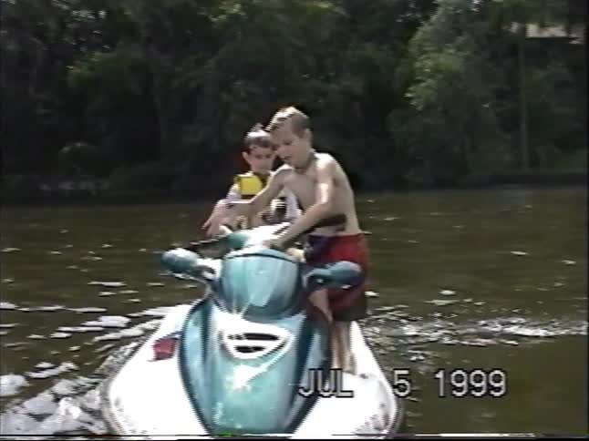 Vintage VHS footage from 1999 shows two young boys and their happy dog posing and riding on a jet ski on a lake