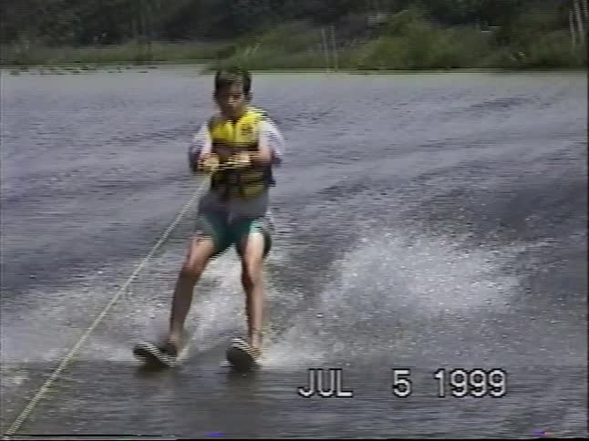 A young boy triumphs as he gets up on water skis and glides across a calm lake in this nostalgic 1999 home video