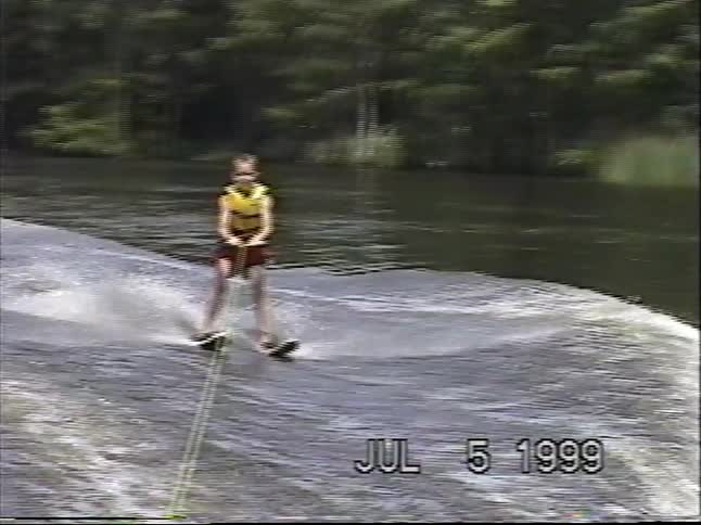 A young boy holds on tight as he water skis across a lake in this vintage home video from 1999