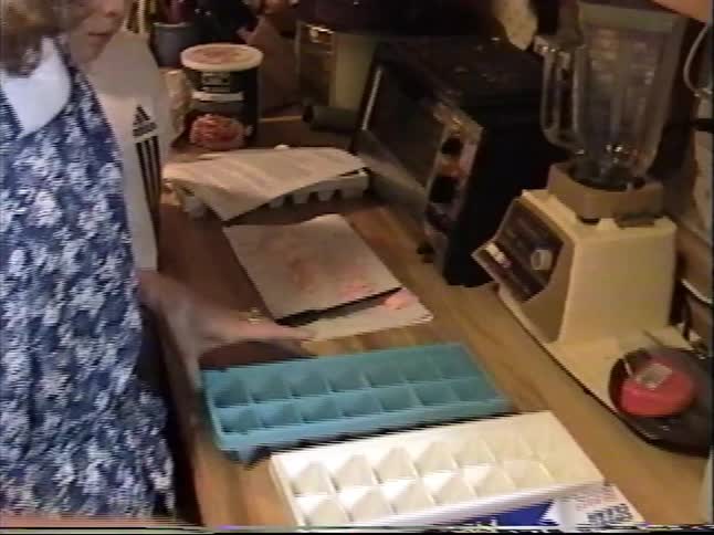 Woman and child prepare ingredients in a home kitchen with ice cube trays and mixing bowls