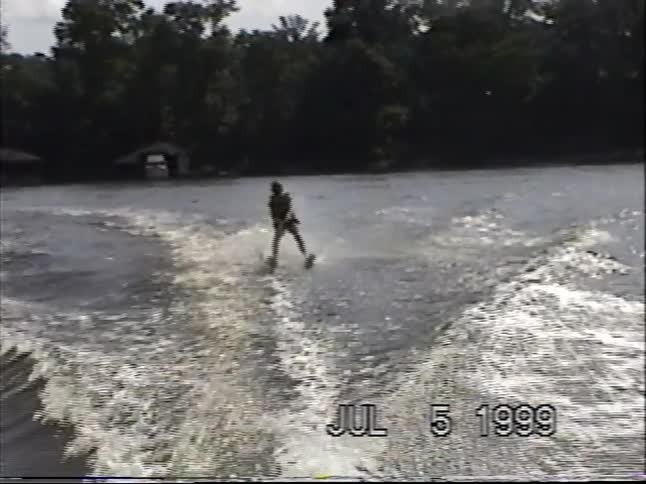 A young child successfully gets up on water skis and glides across a lake in this vintage 1999 home video
