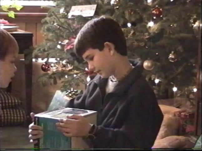 Vintage home video footage shows two young brothers opening their presents on a cozy Christmas morning next to a lit tree