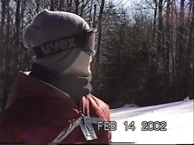 Vintage home video footage shows a young skier standing on a snowy mountain on a sunny day in 2002