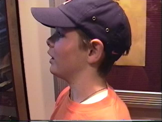 A close-up of a young boy in a baseball cap looking out from inside a descending glass elevator