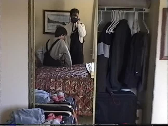 Vintage home video footage shows a man filming himself and a child in a hotel room mirror before a ski trip