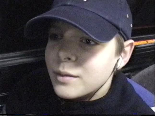 Vintage, grainy footage shows a close-up of a young boy in a baseball cap and earbuds at night