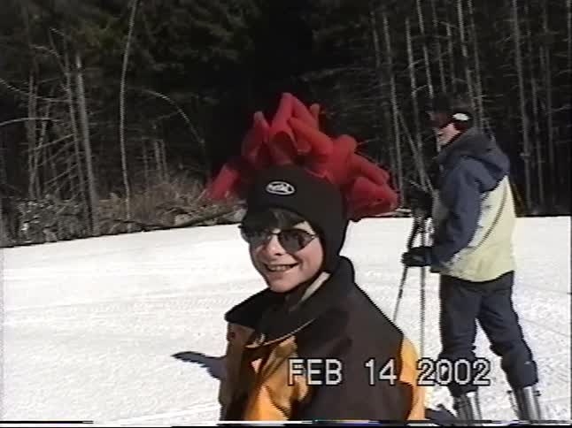 A smiling kid in a wild red hat and sunglasses enjoys a sunny ski day with family in this nostalgic 2002 home video
