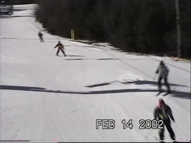 Vintage VHS footage from 2002 captures several people skiing down a sunny mountain slope