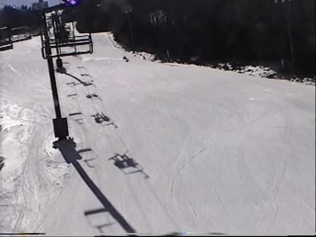 Vintage POV footage from a ski lift captures a serene view of a snowy slope with a lone skier below