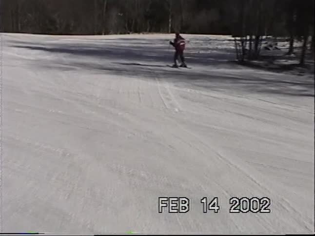 Vintage camcorder footage shows a person skiing down a snowy mountain slope on a sunny winter day