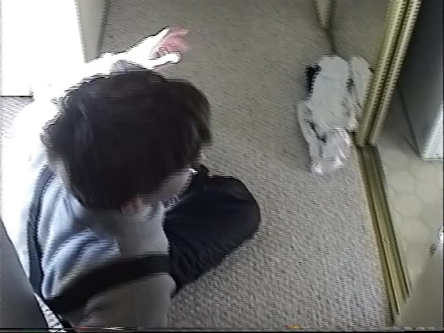 Candid home video footage from the 90s shows a teenage boy sitting on the floor in a sunlit hallway