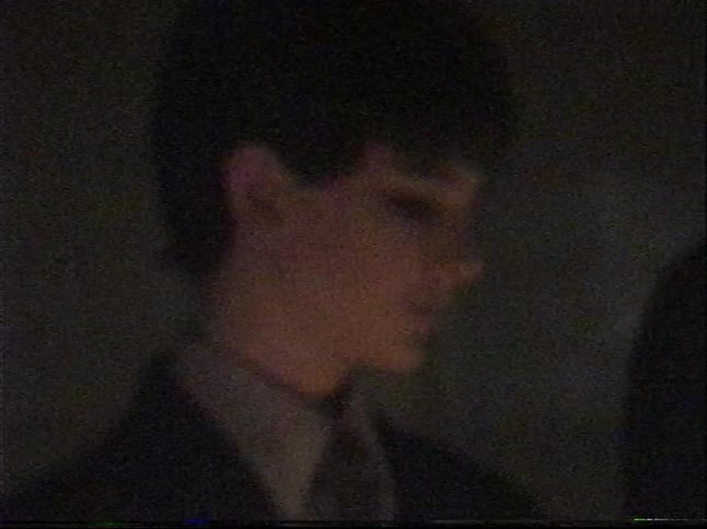 A grainy, vintage close-up of a contemplative young man in a suit, illuminated by warm, dim light