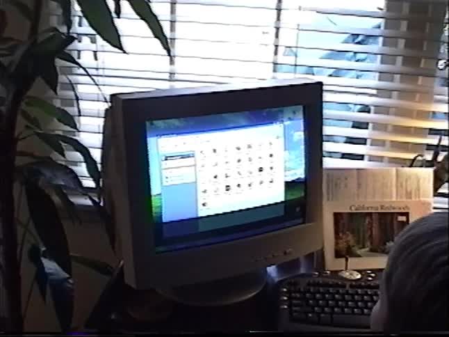 A young boy sits at a desk looking at the screen of an old CRT computer monitor in a home office