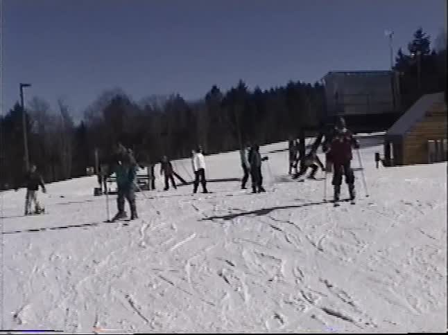 Vintage VHS footage of a group of young people learning to ski and snowboard on a sunny day at a ski resort