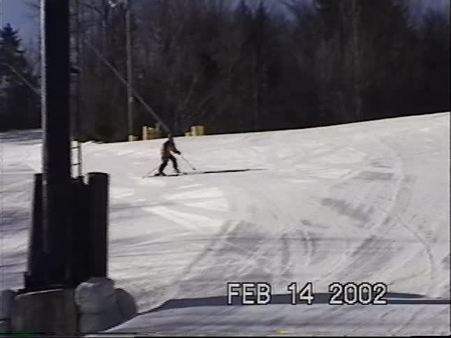 Archival home video from 2002 captures a skier in a bright yellow jacket skillfully navigating down a wide, sunny ski slope