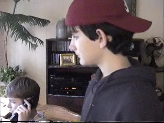 Vintage VHS footage shows two teenage boys in their room, one on an old cell phone and the other standing in a hoodie