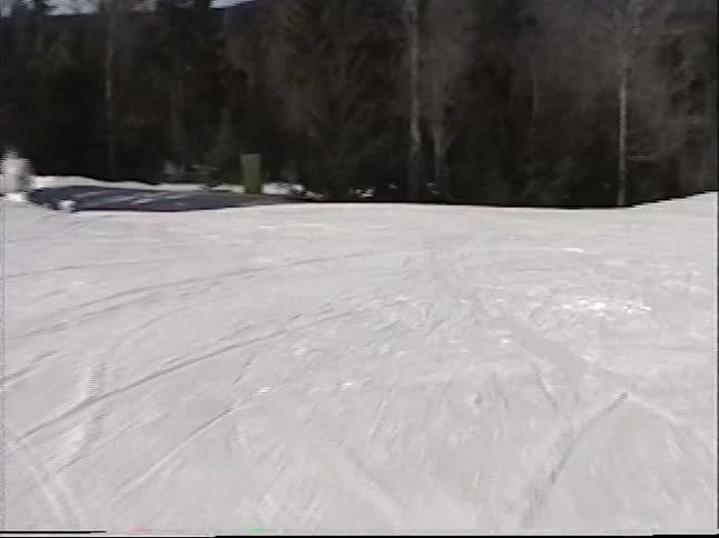 Vintage point-of-view footage follows a skier down a sunny terrain park with jumps next to a chairlift