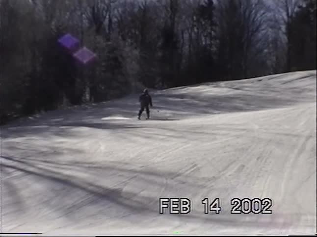 Vintage home video from 2002 shows a skier descending a snowy mountain slope on a sunny winter day