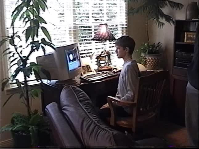 Vintage VHS footage shows a young boy using an old desktop computer at home as his family watches