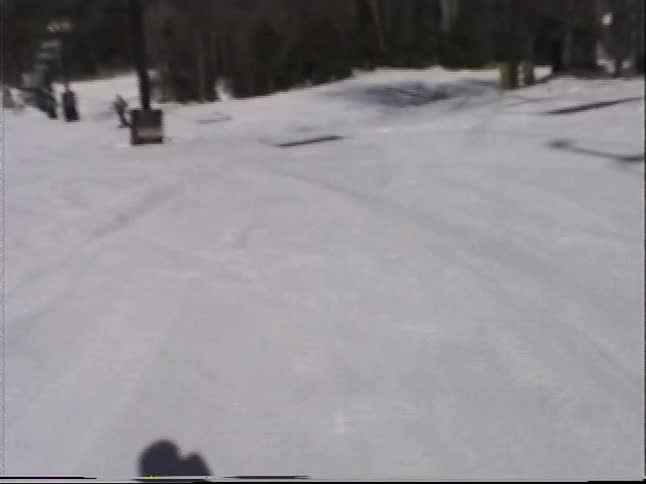 A vintage first-person view captures a skier going down a snowy slope and stopping to talk with a friend