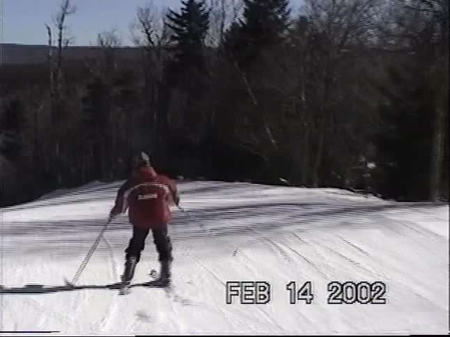 A vintage clip from 2002 shows a person in a red jacket skiing down a groomed mountain trail on a sunny day